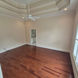Empty room with wood floors, a ceiling fan, tray ceiling, neutral walls, and a doorway leading to another room.