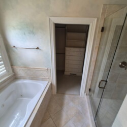 Bathroom with a bathtub, glass shower door, tile floor, and an open door leading to a walk-in closet with shelves.