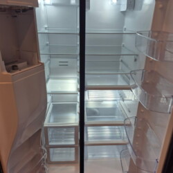 An open, empty refrigerator and freezer with clear shelves and door compartments, illuminated by interior lights.