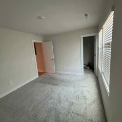 Empty carpeted room with white walls, a window with blinds, an open door, and a small closet.