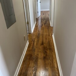 A hallway with polished wooden floors, beige walls, white trim, and doors leading to other rooms.
