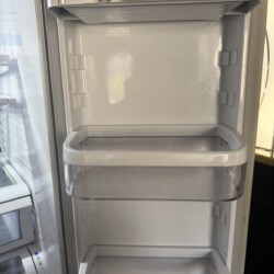 The open door of a refrigerator showing three empty, clear plastic shelves against a white interior.